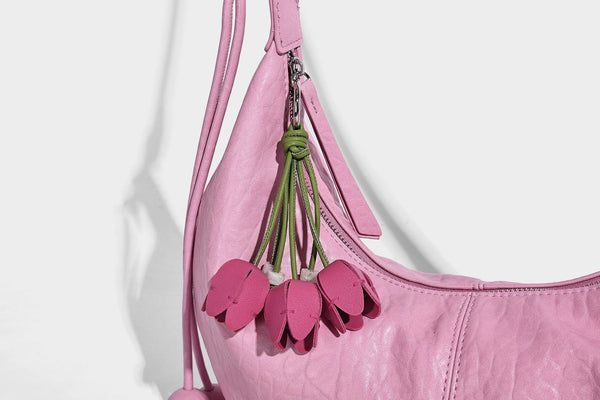Slouchy crescent half-moon shoulder bag in pink pebbled textured finish with floral charm and knotted side detail, detail