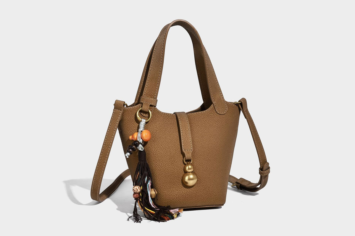 Kleine matte Beuteltasche mit genarbter Oberfläche, antikgoldfarbenen Ringbeschlägen, Perlen- und Quastenanhänger, kurzen Tragegriffen oben und