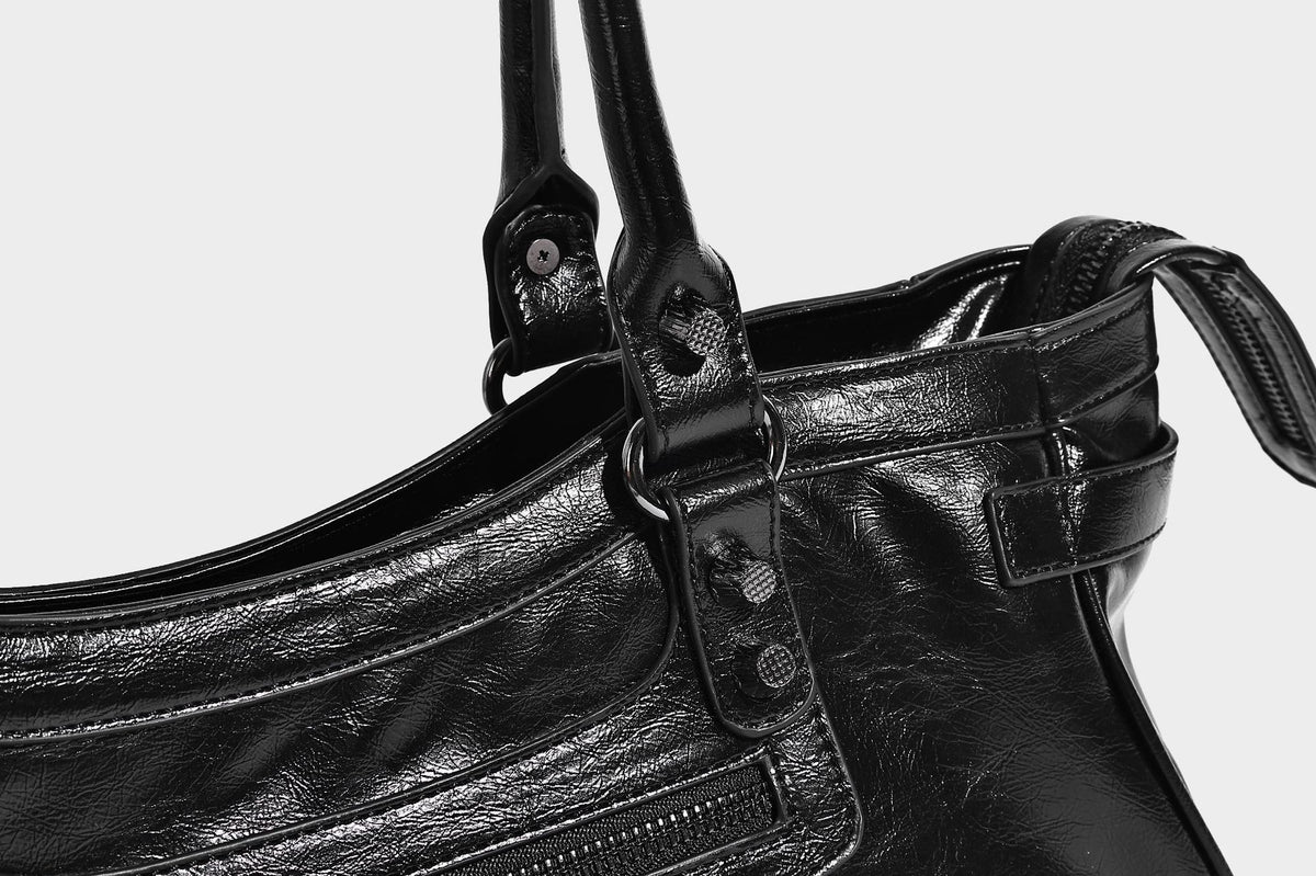 Längliche Schultertasche in Zylinderform mit glänzender Lederoptik, silberfarbenen Nietenbeschlägen, seitlichen Quasten und mehreren außenliegenden Reißverschlüssen