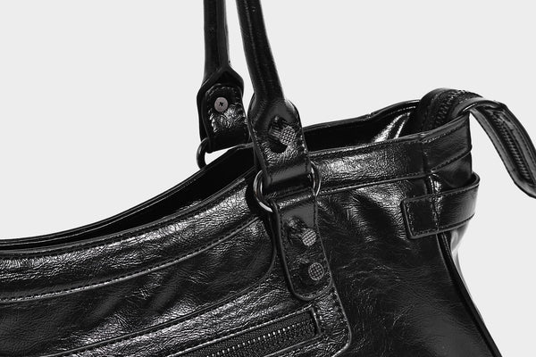 Längliche Schultertasche in Zylinderform mit glänzender Lederoptik, silberfarbenen Nietenbeschlägen, seitlichen Quasten und mehreren außenliegenden Reißverschlüssen