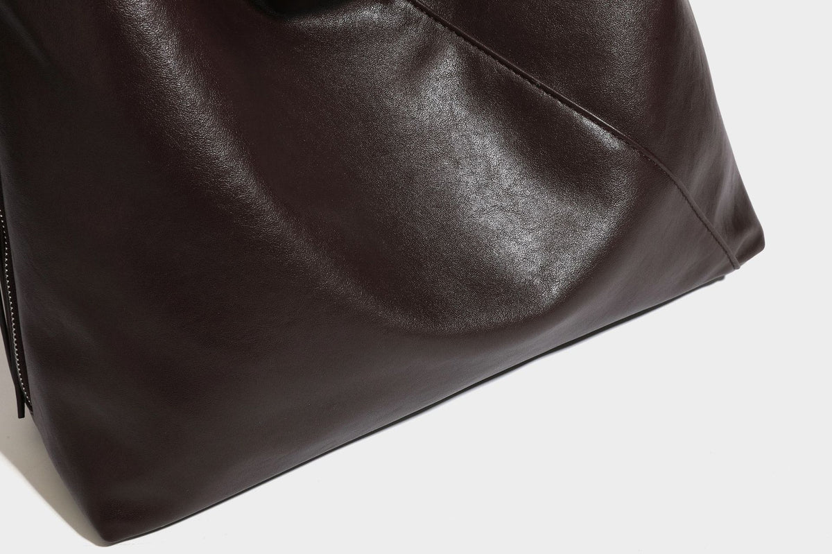 Large slouchy hobo shoulder bag with braided top handle, smooth glossy leather-look finish, and silver-tone ring hardware