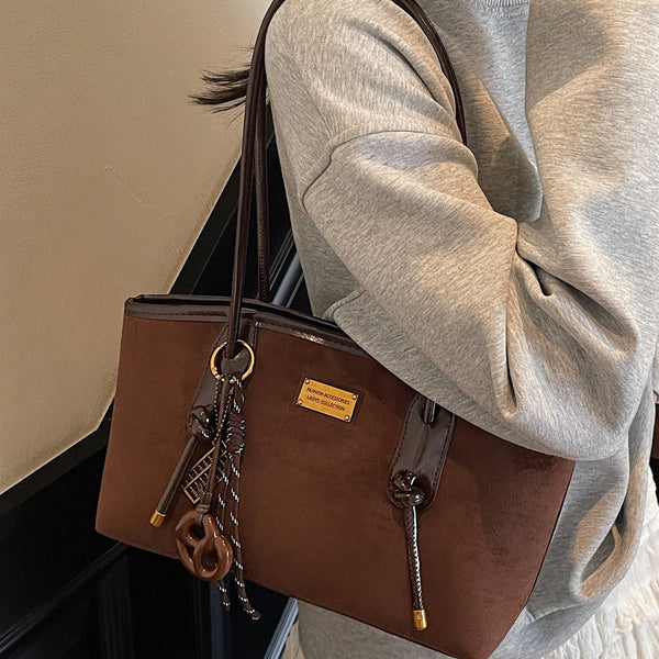 Structured suede-finish tote bag with glossy black leather-look trim, dual top handles, and decorative hanging charm in