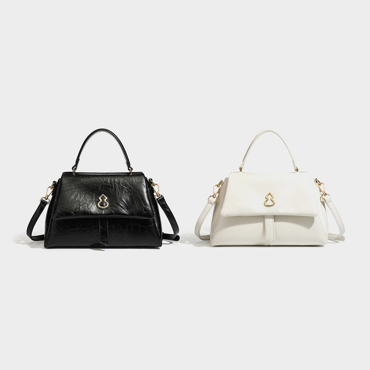 Structured black satchel bag with glossy crinkled leather-look finish, gold-tone emblem flap closure, slim top handle, and