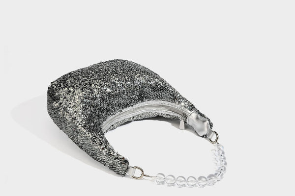 Kleine sichelförmige Schultertasche mit vollständig mit silberfarbenen Pailletten besetzter Außenseite, transparentem Henkel aus kugelförmigen Perlen und Reißverschluss in Silberoptik
