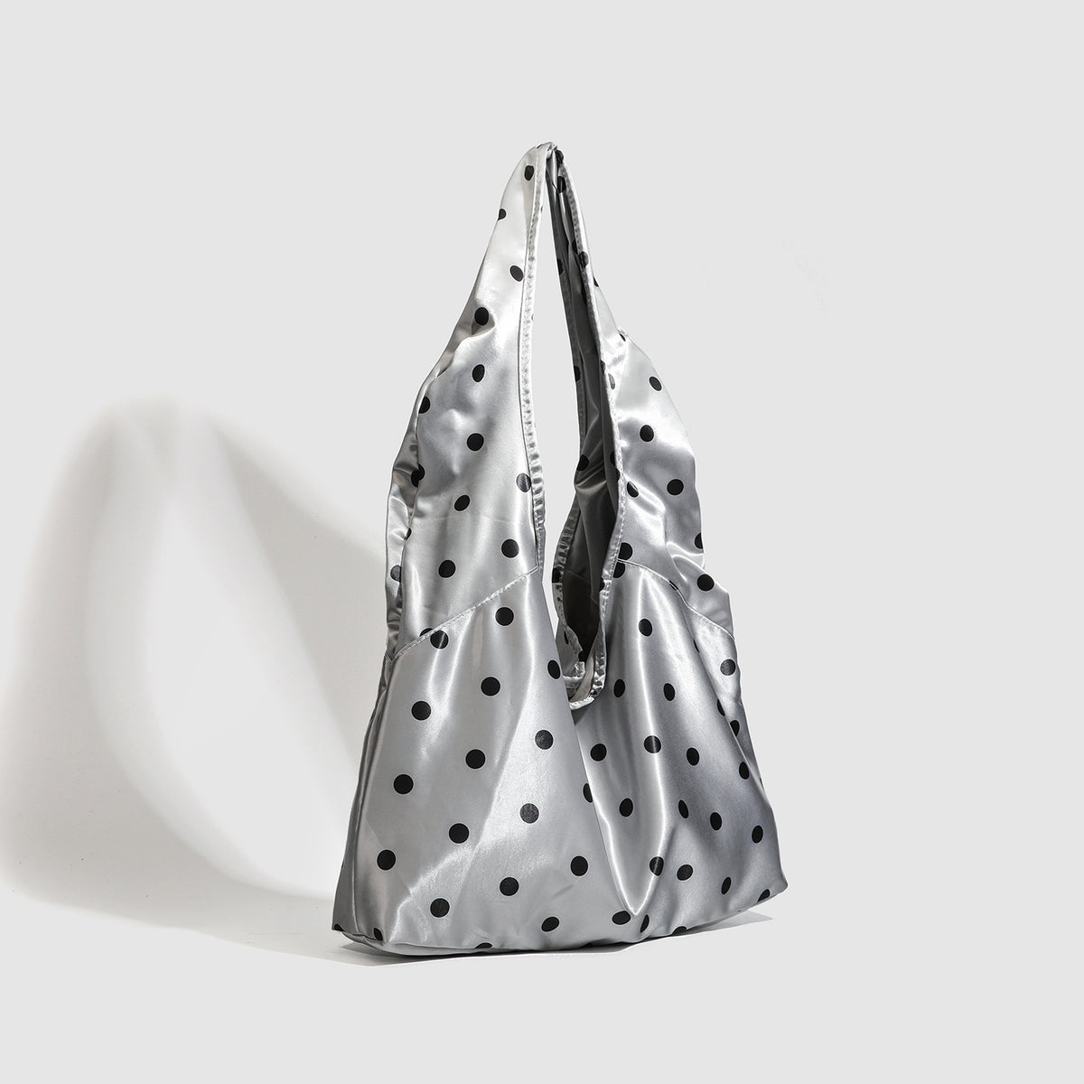 Silver satin-like oval tote shoulder bag with black polka-dot print, snap closure, and long integrated straps, detail view 2