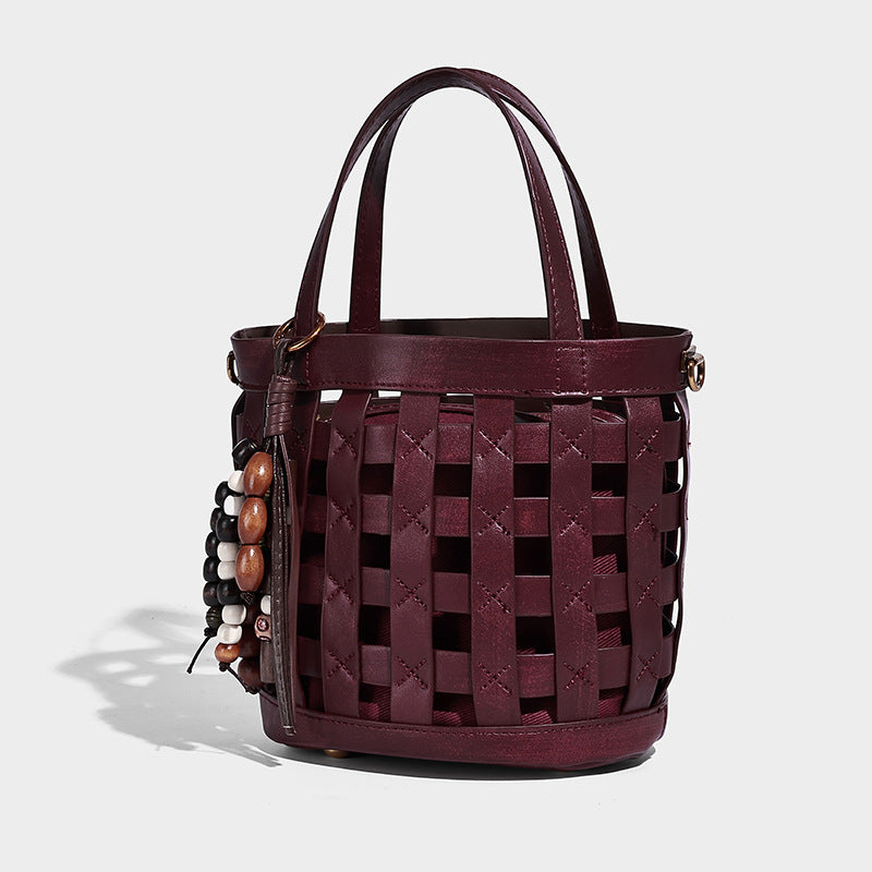 Small woven lattice bucket bag in brown leather-look finish with beaded tassel charm, dual top handles, and detachable