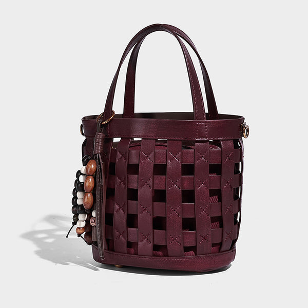 Small woven lattice bucket bag in brown leather-look finish with beaded tassel charm, dual top handles, and detachable