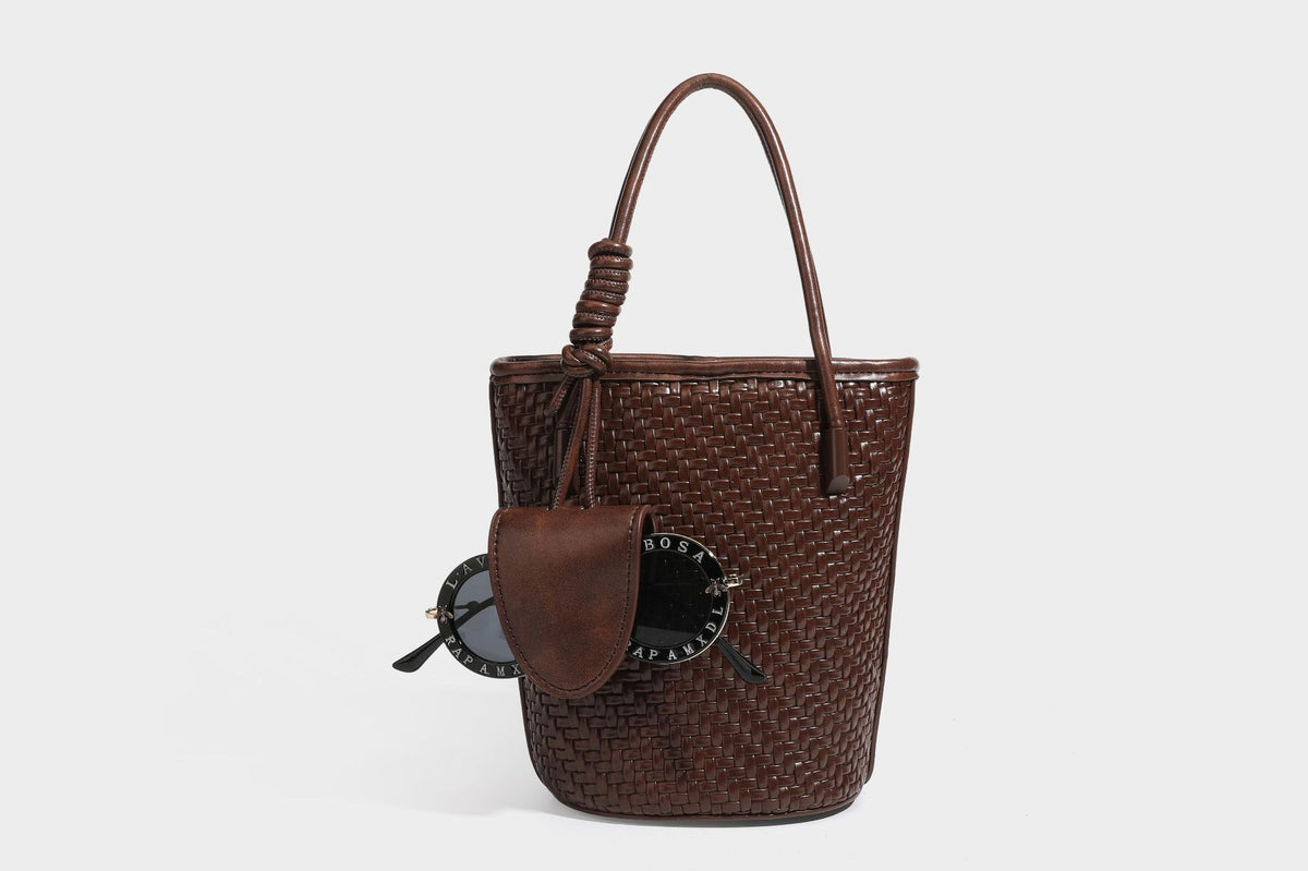 Structured woven-texture leather-look bucket bag in brown with knotted top handles, small front flap pouch, and adjustable