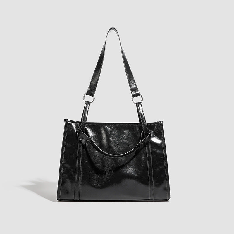 Large structured glossy leather-look tote bag with dual top handles and long shoulder strap in burnished brown, detail view 7
