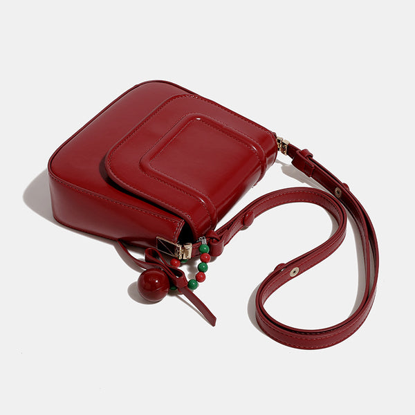 Mini-Satteltasche in glänzender Lederoptik zum Umhängen mit Überschlagverschluss, goldfarbenen Metalldetails und Perlenanhänger, Detailansicht 4