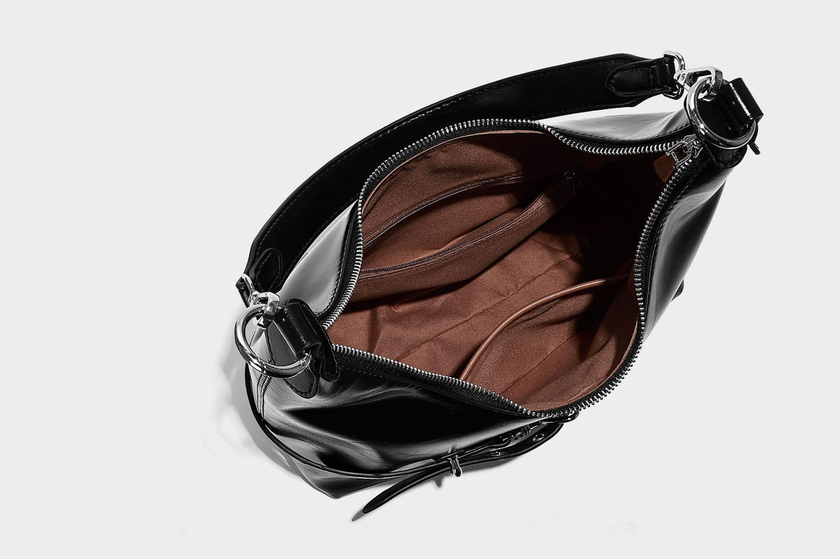 Glossy black slouchy hobo shoulder bag with silver-tone hardware, belt-style grommet strap at base, and long adjustable