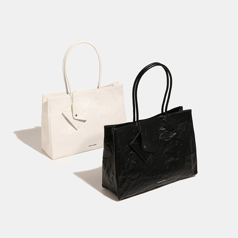 Large glossy crinkled rectangular tote bag with long double handles and hanging envelope snap tag, detail view 2