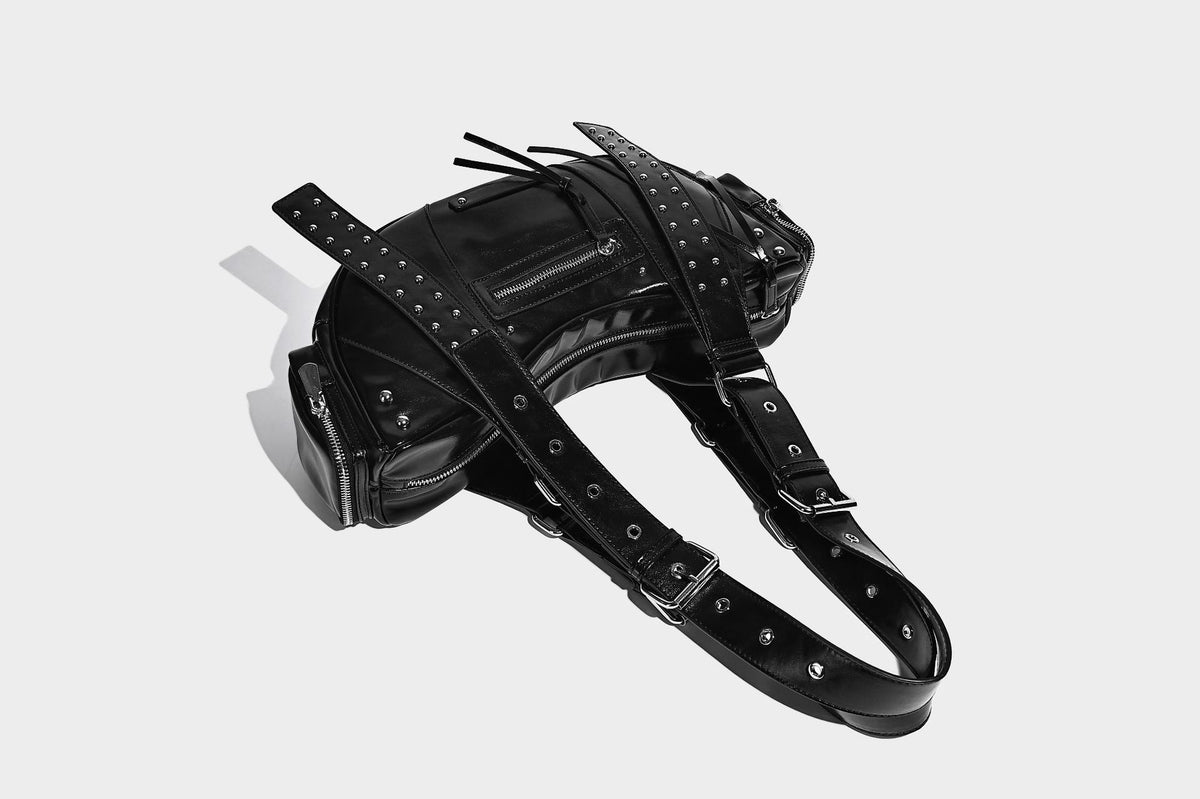 Glossy black crescent shoulder bag with silver-tone rivets, multiple zip pockets, and long adjustable studded straps, detail
