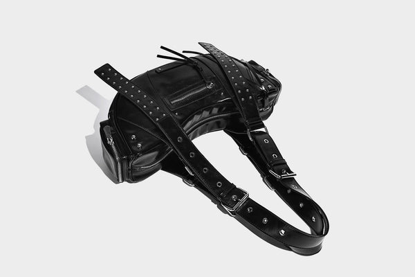 Glossy black crescent shoulder bag with silver-tone rivets, multiple zip pockets, and long adjustable studded straps, detail