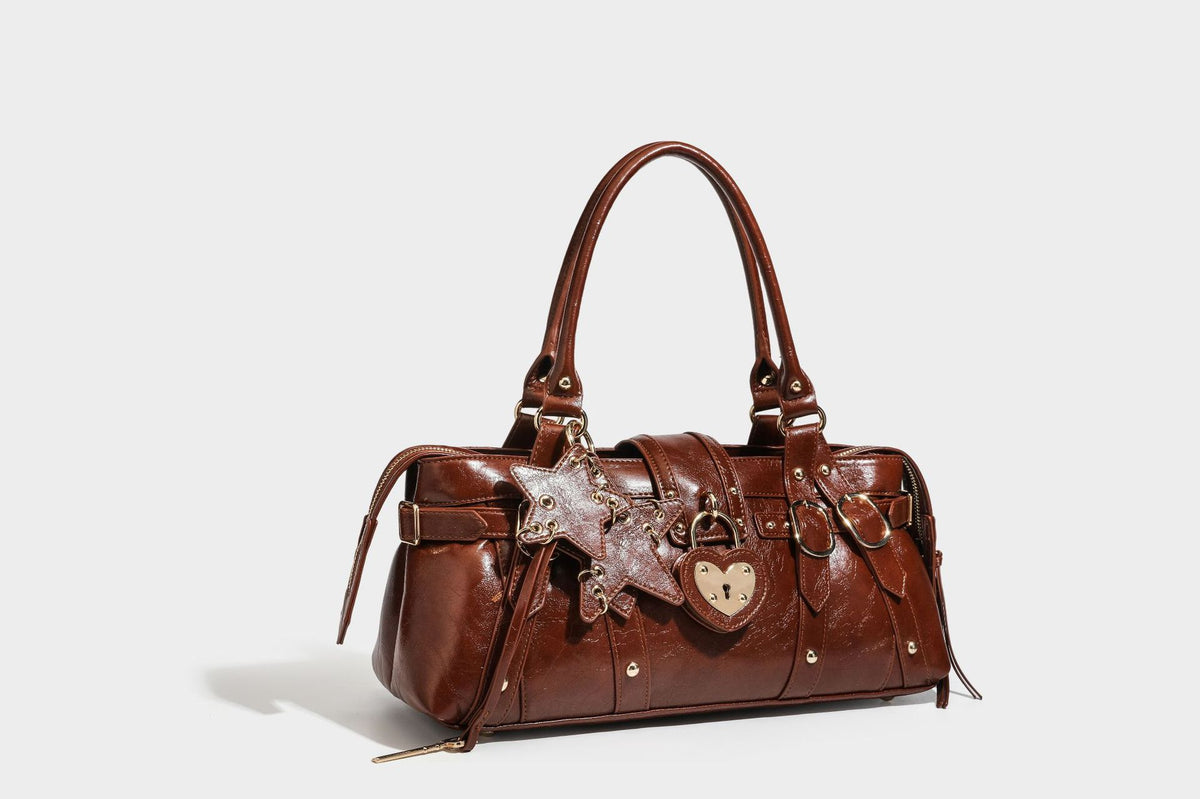 Glossy dark brown structured Boston satchel with heart-shaped lock charm, star pendant, rivet studs, multi-strap front panel