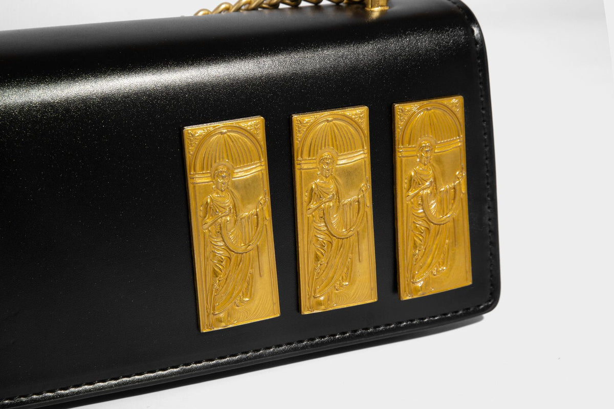 Structured rectangular crossbody bag with glossy finish, three vertical gold-tone embossed plaques, and gold chain strap