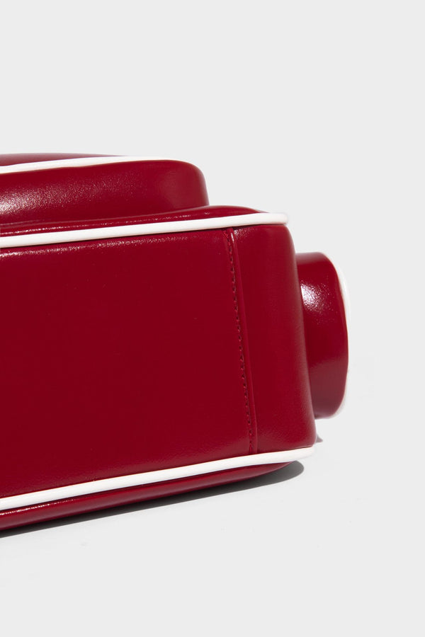 Kleine, formstabile, glänzende Schultertasche mit weißer Paspelierung, Spitzenschleife und Anhänger mit roter Perle, seitlichen Reißverschlusstaschen und silberfarbenem