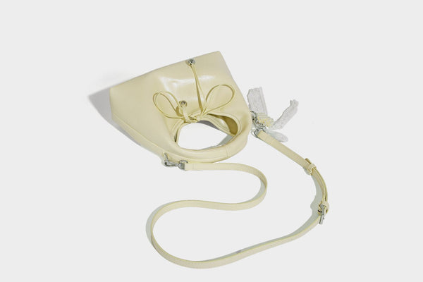 Kleine kuppelförmige Henkeltasche in glänzender Lederoptik mit Kordelzugverschluss, weißem Spitzen-Schleifenanhänger und silberfarbenen Metallbeschlägen
