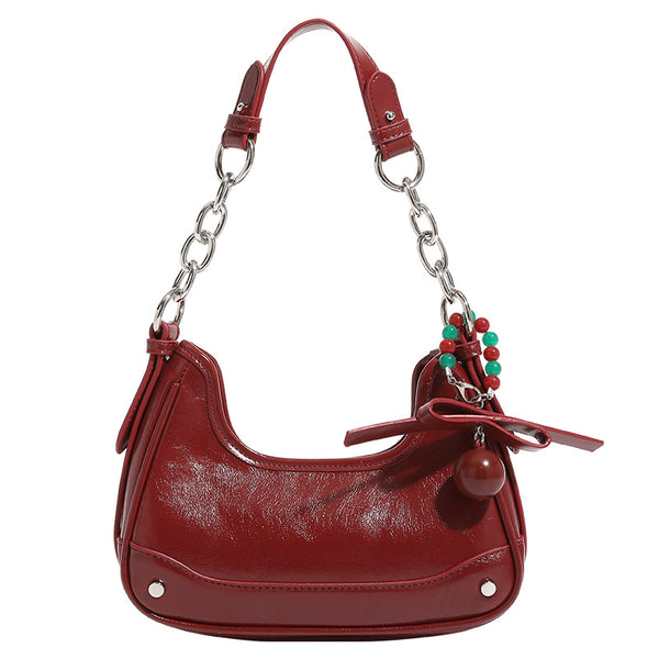 Small glossy cherry red crescent shoulder bag with silver chain strap, bead and tassel charm, and round pendant, detail view