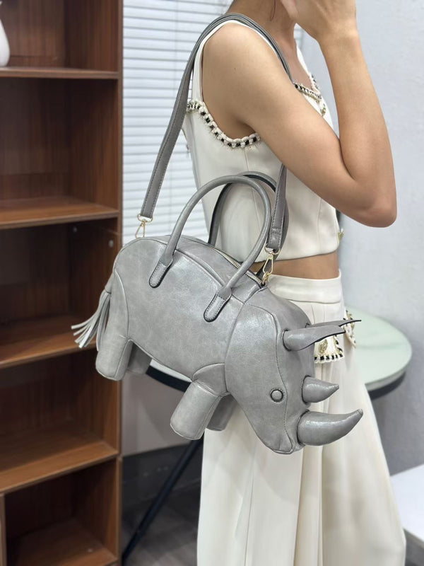 Rhinoceros-shaped 3D structured handbag with sculpted horns, four legs, tassel tail, twin top handles, and detachable, detail