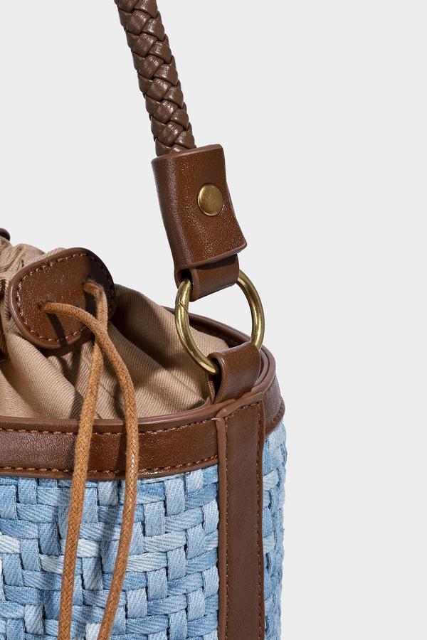 Small light blue woven bucket bag with brown leather-look trim, braided top handle, brass-tone ring hardware, drawstring