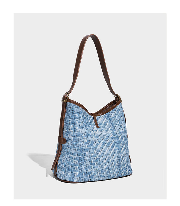 Light blue woven bucket bag with brown leather-look trim, gold-tone hardware, adjustable shoulder strap, and decorative bead