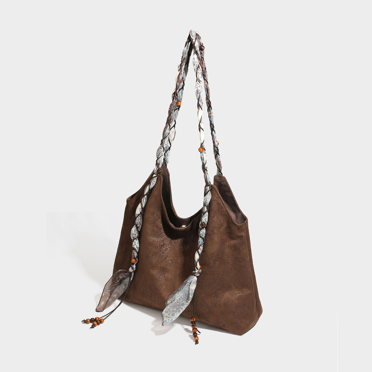 Slouchy paisley-embossed suede-look shoulder tote bag with braided patterned fabric straps and wood bead accents, detail view