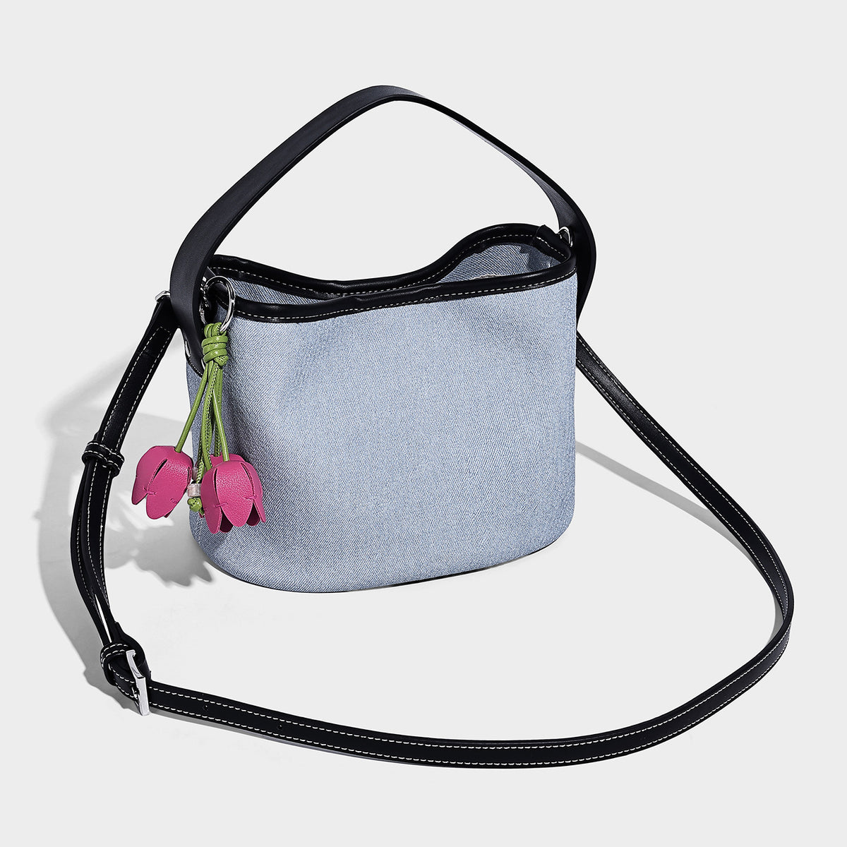 Light blue denim bucket bag with black leather-look trim, silver-tone hardware, short top handle, long adjustable crossbody