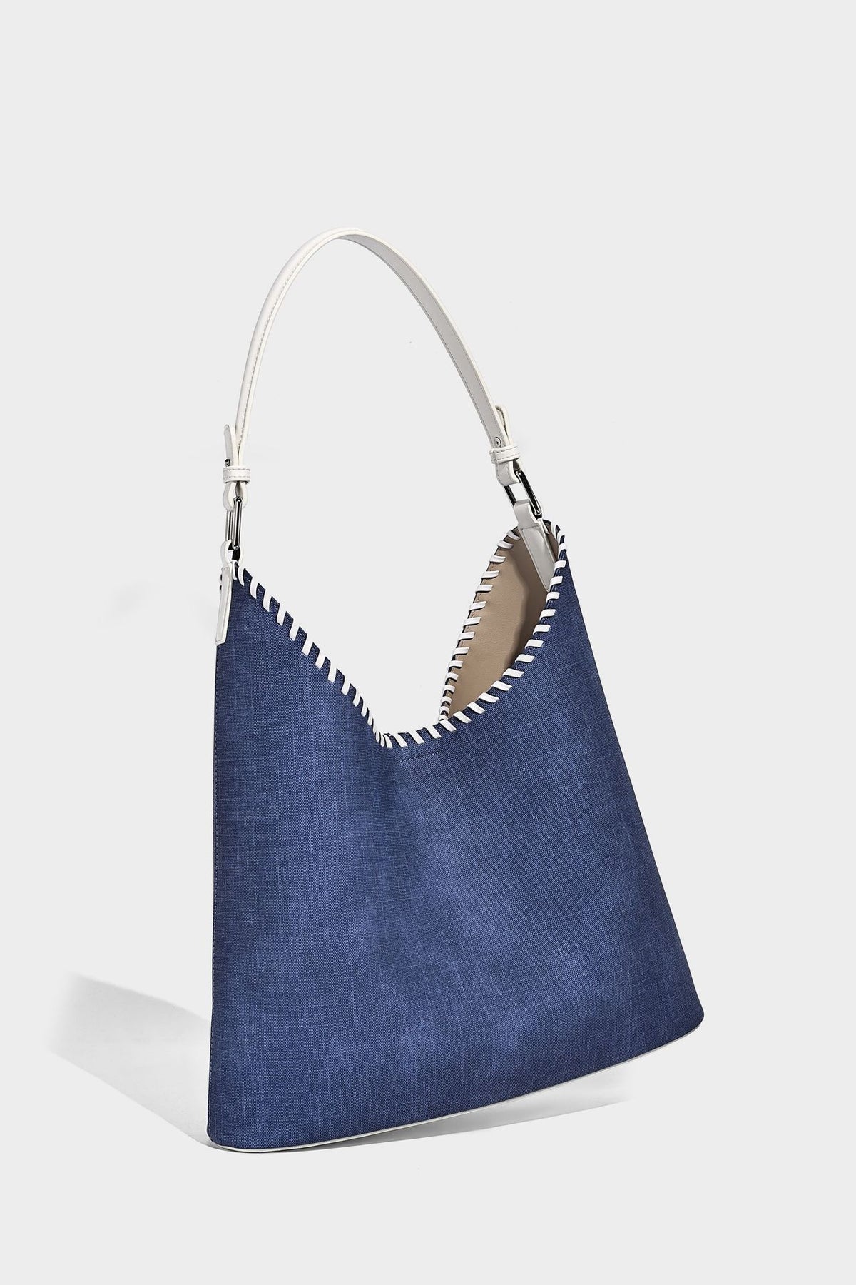 Denim-blue hobo tote with white leather-look shoulder strap, contrast whipstitch trim along curved open top, and silver-tone