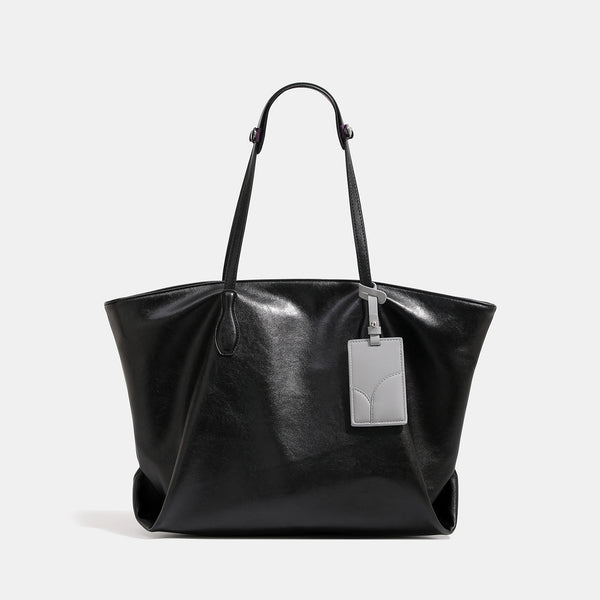Large soft trapezoid tote bag with leather-look finish, dual shoulder straps, and gray hanging card tag, front view