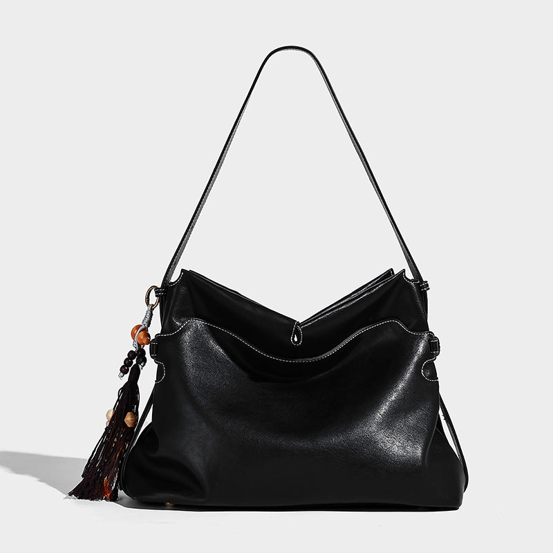 Large slouchy leather-look hobo tote bag with open top, adjustable shoulder strap, and colorful tassel bead charm, detail