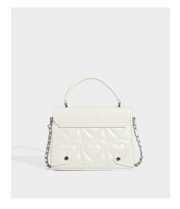 Kleine strukturierte Box-Tasche aus herzförmig gestepptem PU mit Henkel, silberfarbenem Kettenriemen zum Tragen als Crossbody und ovalem Drehverschluss, Detailansicht