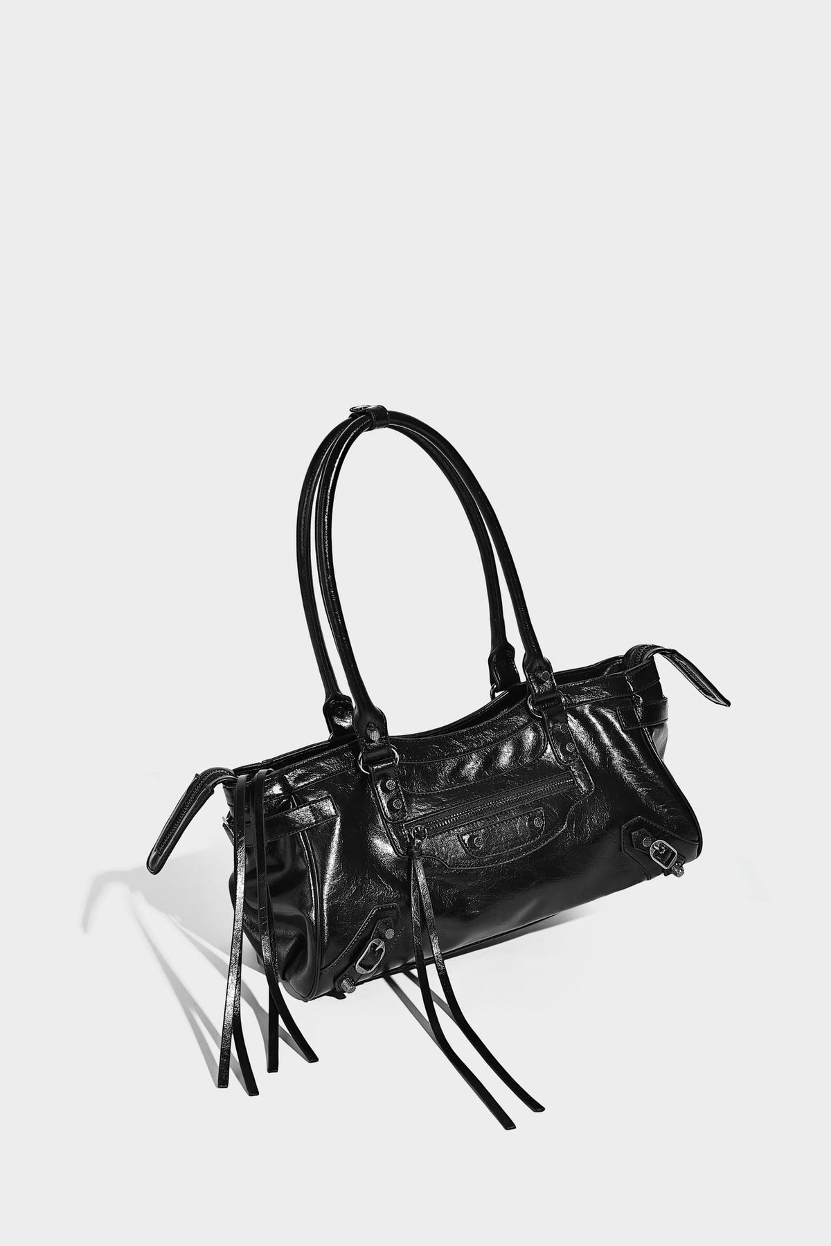 Längliche Schultertasche in Zylinderform mit glänzender Lederoptik, silberfarbenen Nietenbeschlägen, seitlichen Quasten und mehreren außenliegenden Reißverschlüssen