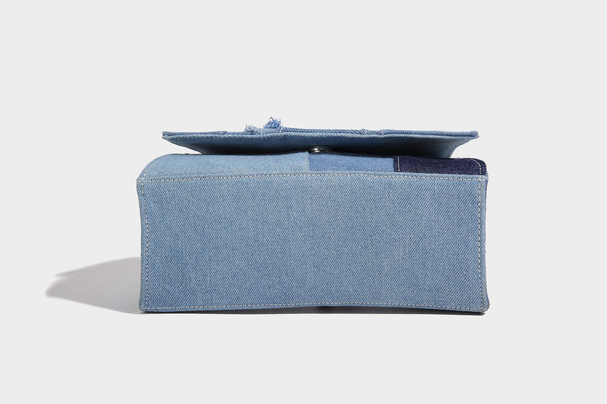 Structured patchwork denim trapezoid satchel bag with frayed panel trim, rounded top handle, and silver-tone hardware, detail