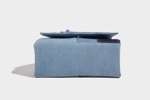 Structured patchwork denim trapezoid satchel bag with frayed panel trim, rounded top handle, and silver-tone hardware, detail