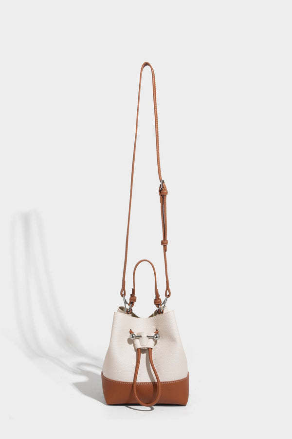 Small two-tone pebbled drawstring bucket bag with tan contrast base, metal toggle hardware, short top handle, and detachable