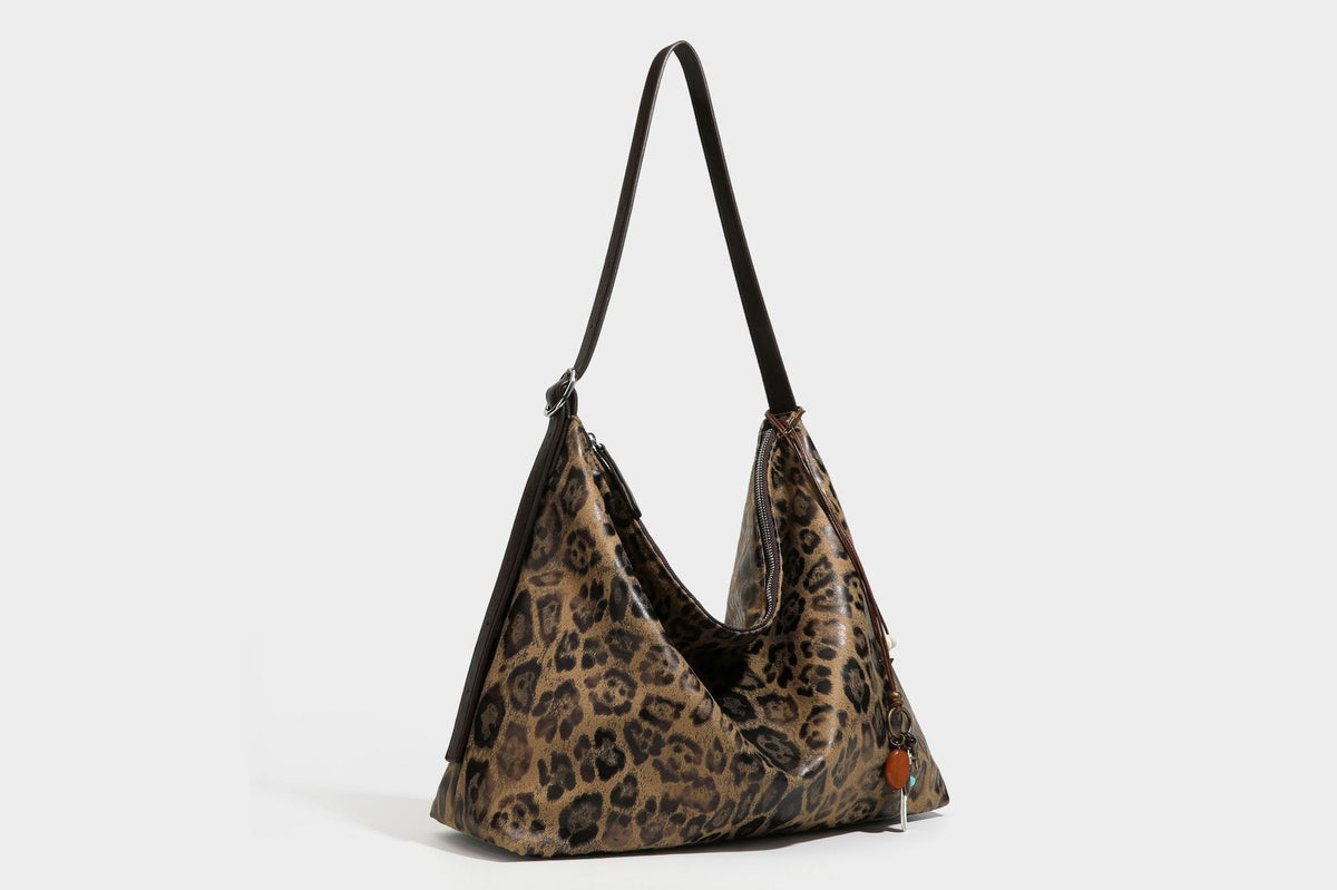 Slouchy leopard print hobo shoulder bag with glossy coated finish, top zipper closure, dark brown trim, and dangling charm