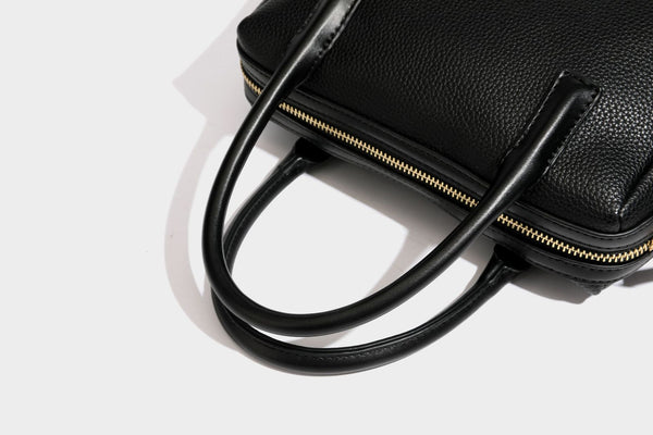 Small structured pillow satchel bag with pebbled leather-look finish, dual rolled top handles, gold-tone gourd emblem, and