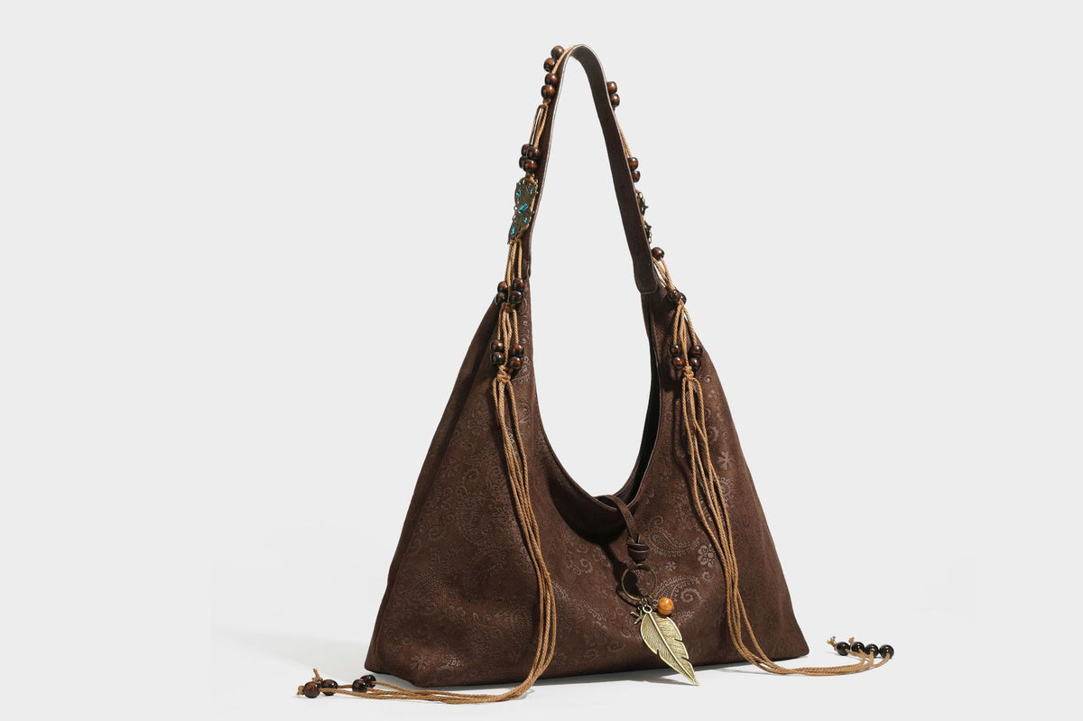 Slouchy boho hobo shoulder bag in embossed brown suede-look finish with beaded strap, cord tassels, and brass-tone leaf
