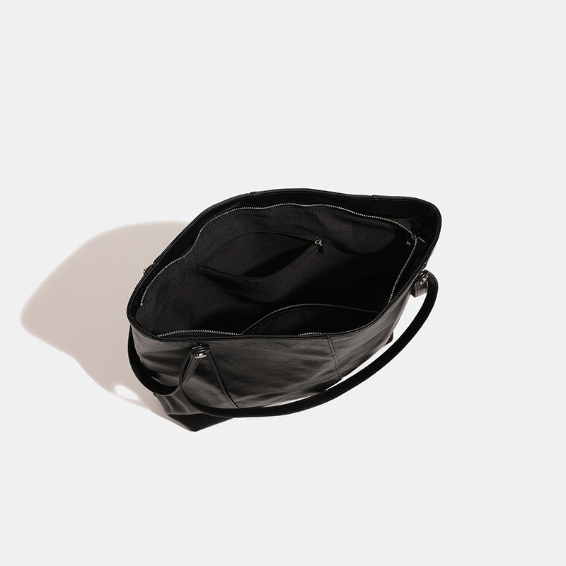 Große quadratische Shopper-Tasche in schwarzer Lederoptik mit zwei Schultergriffen und längerem Trageriemen, glatte glänzende Oberfläche und seitliche Beschläge