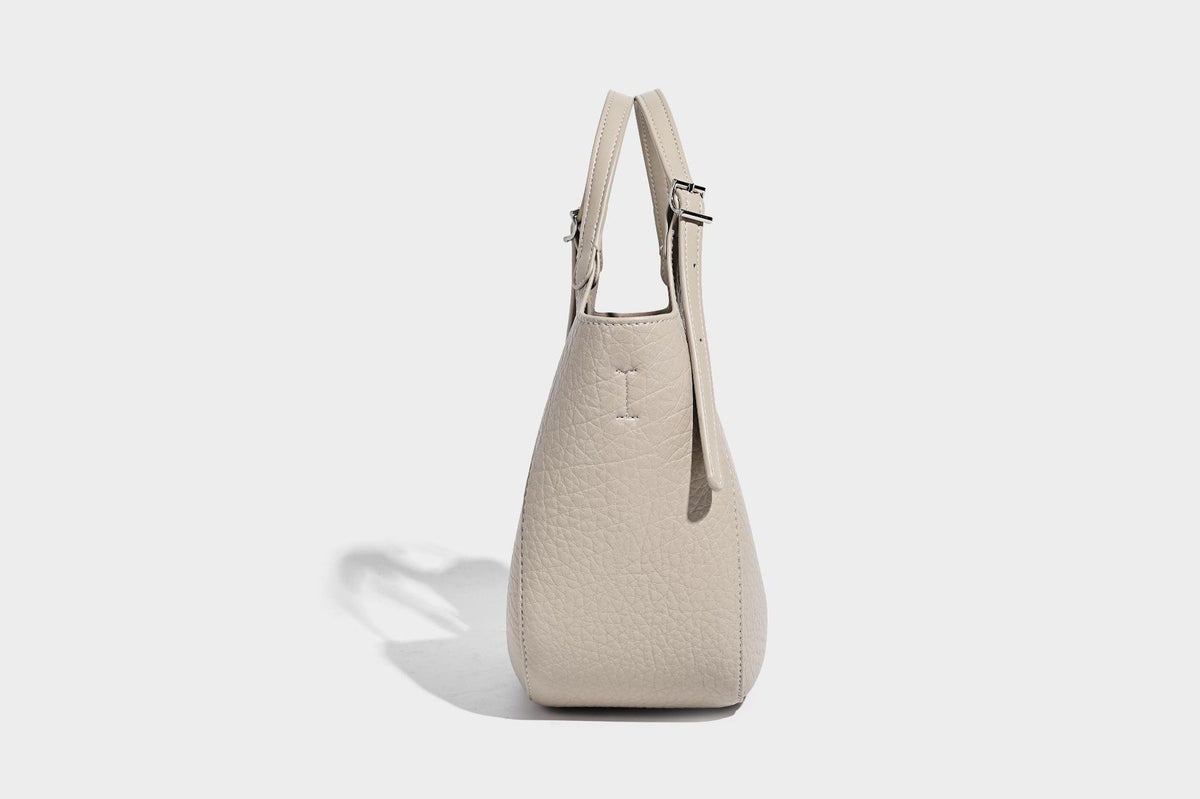Small pebbled half-moon shoulder bag with dual top handles, detachable crossbody strap, and silver-tone hardware, detail view