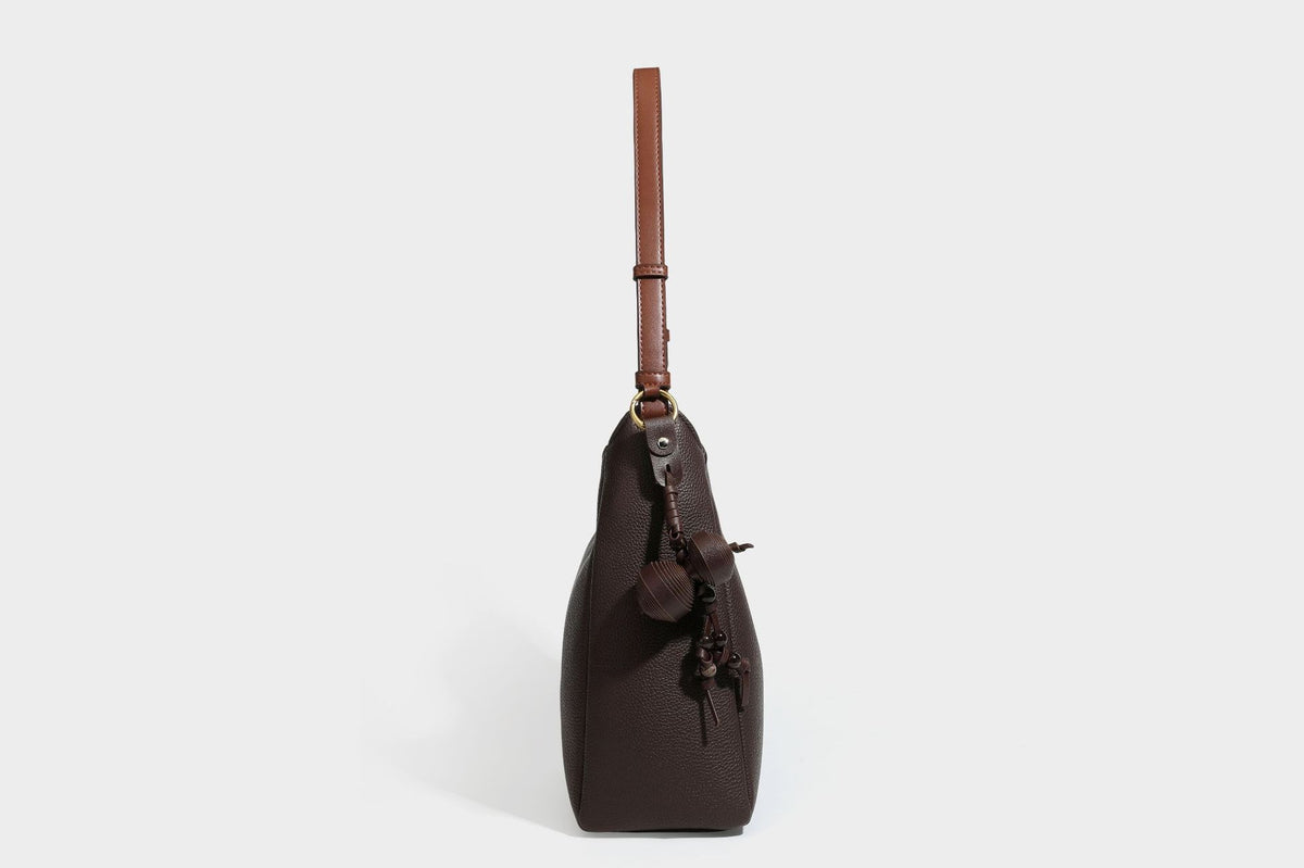 Hobo-Schultertasche in dunklem Espresso mit genarbter Oberfläche, warmen cognacfarbenen Details, verstellbarem schmalem Riemen, goldfarbenen Ringbeschlägen und geknotetem