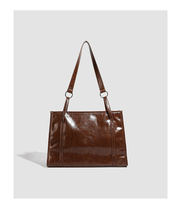 Large structured glossy leather-look tote bag with dual top handles and long shoulder strap in burnished brown, detail view