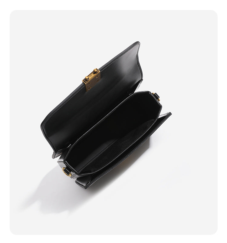 Mini structured black flap crossbody bag with gold-tone ribbed rectangular clasp and adjustable shoulder strap, detail view