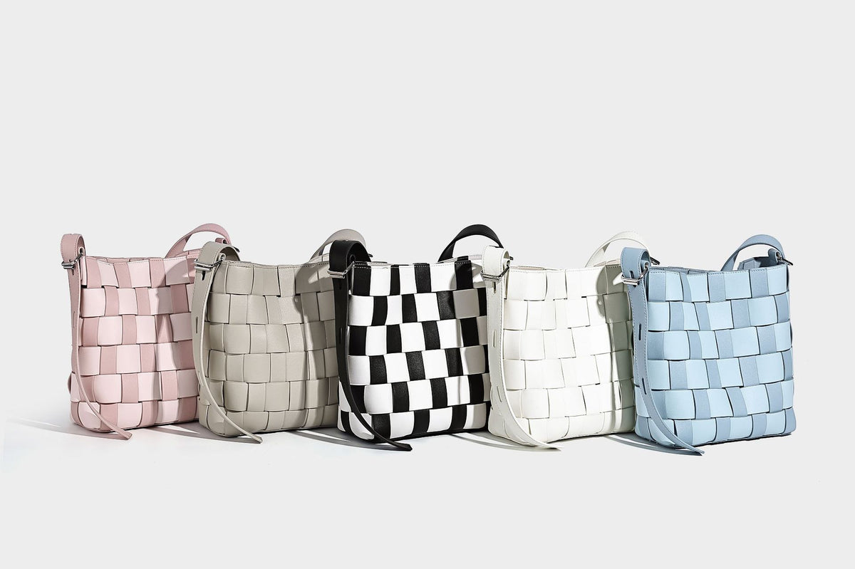 Hand-woven black-and-white checkerboard bucket bag with smooth black trim, silver-tone ring hardware, and adjustable