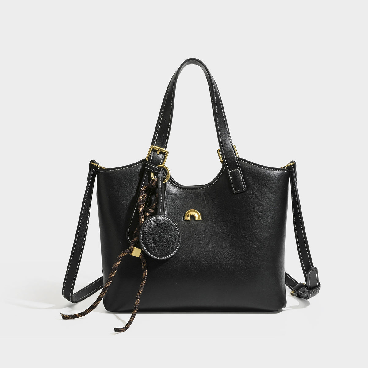 Structured smooth leather-look tote bag with long shoulder strap, gold-tone hardware, and hanging tassel-coin charm, detail