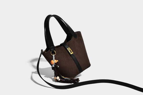Small structured trapezoid tote bag in matte suede-look finish with black contrast trim, gold-tone front clasp, tassel charm