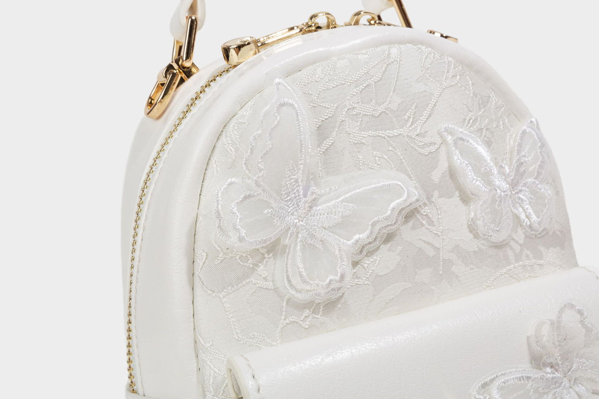 Structured mini backpack handbag with butterfly embroidery, gold-tone chain strap, and turn-lock front flap pocket, detail
