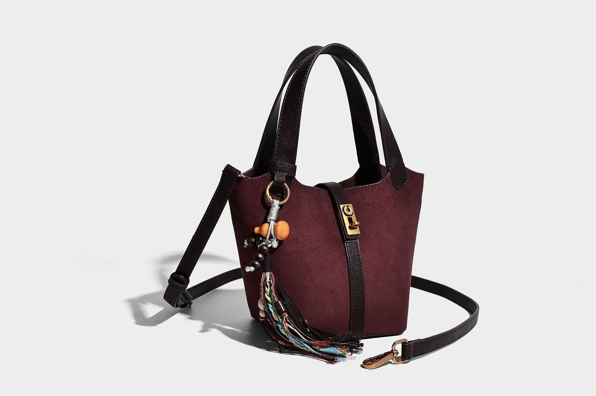 Small structured trapezoid tote bag in matte suede-look finish with black contrast trim, gold-tone front clasp, tassel charm