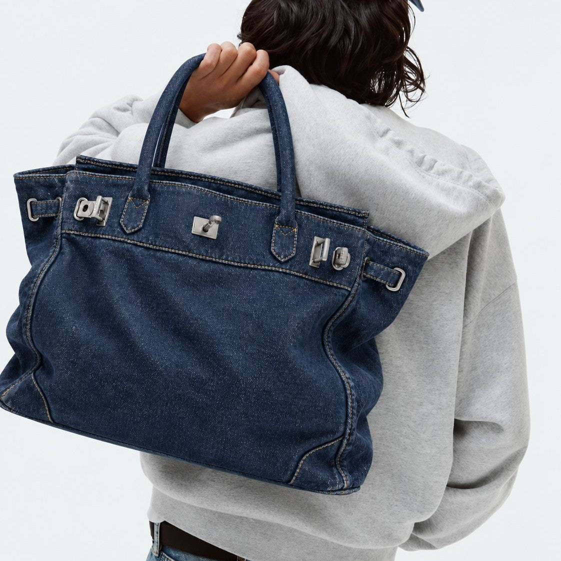Slouchy denim tote bag with silver-tone turn-lock and buckle hardware and dual rolled handles, front view